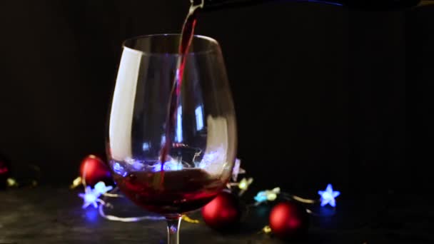 Einschenken von Rotwein in ein Glas auf dem dunklen festlichen Hintergrund mit buntem Bokeh — Stockvideo