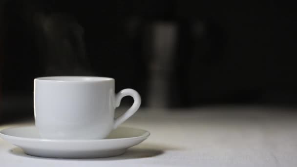 Vapor vem de uma xícara de café, que fica em uma mesa, em um fundo preto — Vídeo de Stock