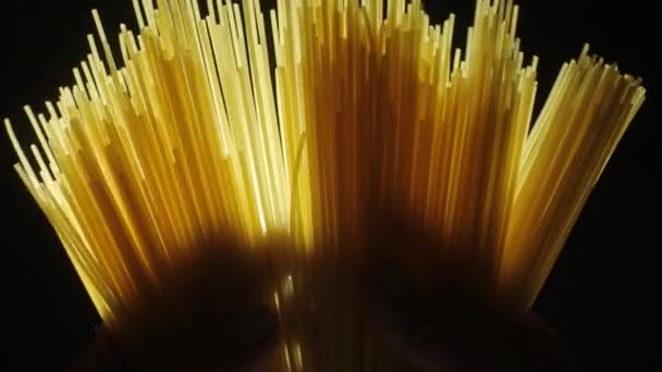 Чоловік тримає золотистий колір сирої пасти спагеті на темно-чорному тлі — стокове відео