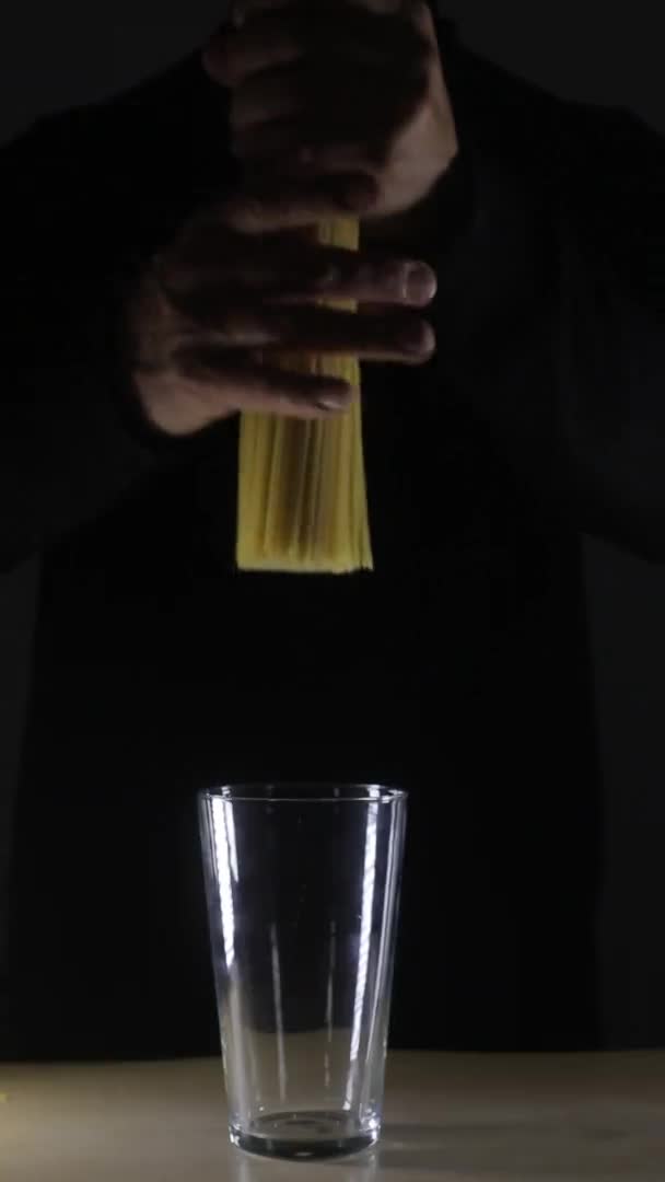 Vertical video. Man holds golden color raw spaghetti pasta on the dark black background — ストック動画