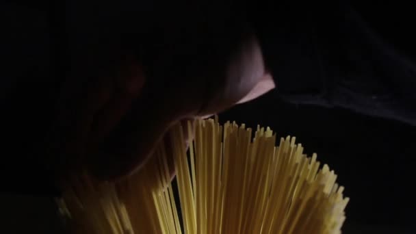Man touches golden color raw spaghetti pasta on the dark black background — Stock Video