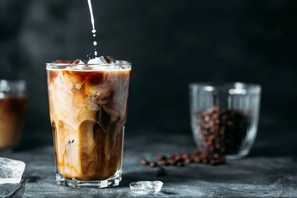 Milch wird in Eiskaffee auf einem dunklen Tisch gegossen — Stockfoto