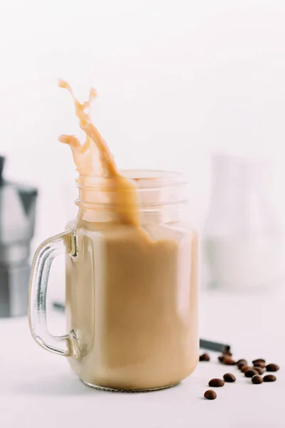 Schizzo di caffè freddo in barattolo di vetro e chicchi di caffè . — Foto Stock