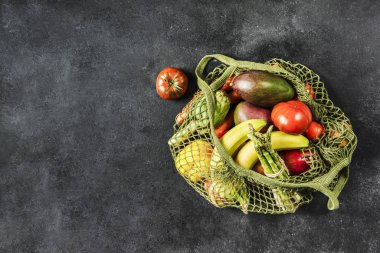 Fresh vegetables and fruits in a green string bag on a black bac