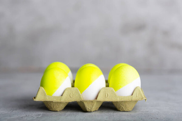 Six yellow painted eggs in tray on a gray concrete background