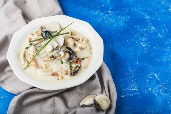Clam chowder in a white plate. The main ingredients are shellfish, broth, butter, potatoes and onions.