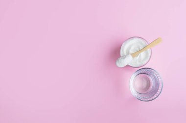 Cam bir su ve pembe zemin üzerinde kolajen tozu olan bir kaşık..