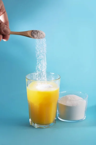 Un zumo de vidrio y una cuchara con polvo de colágeno sobre fondo azul . — Foto de Stock