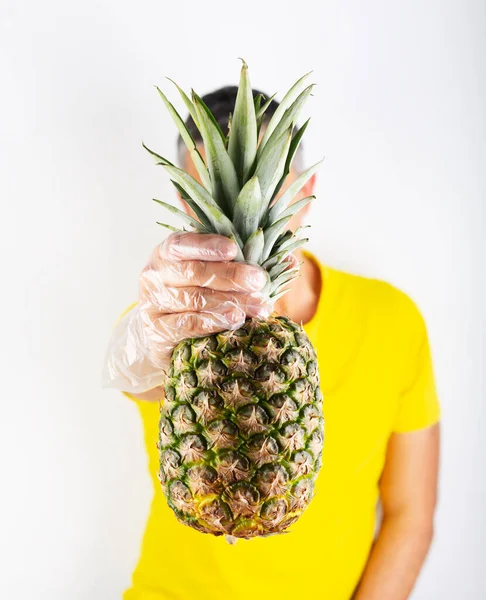 A man in yellow t-shirt wears supermarket gloves and holds ananas. Safety buying — Stock Photo, Image