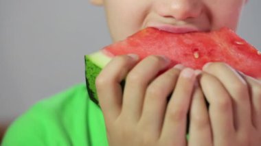 Çocuk kırmızı karpuzu ısırıyor ve çiğniyor.