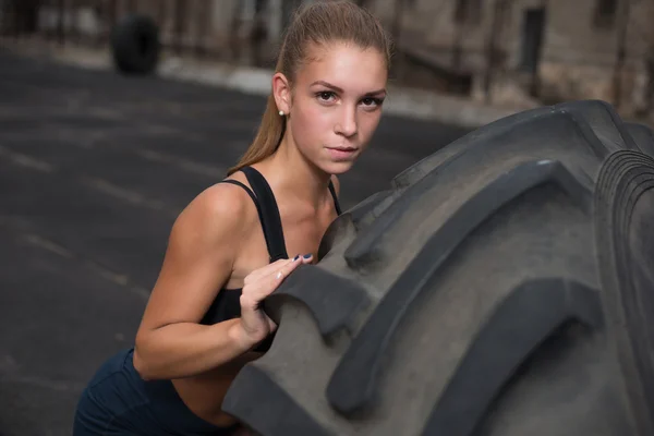 Mięśni młoda kobieta Przerzucanie opony siłowni. Fit lekkoatletka wykonywanie Przerzucanie opony o siłownię crossfit. — Zdjęcie stockowe