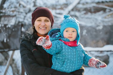 anne kucağında küçük bir çocuk duruyor. Karlı kış parkta bir yürüyüş.