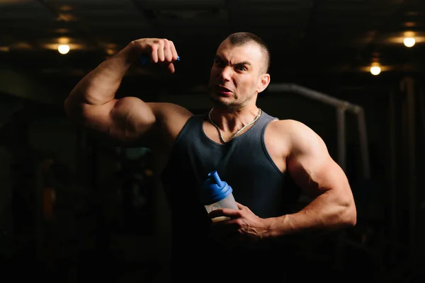 Yakışıklı ve kaslı bir adam, spor salonunda kameraya poz veriyor.