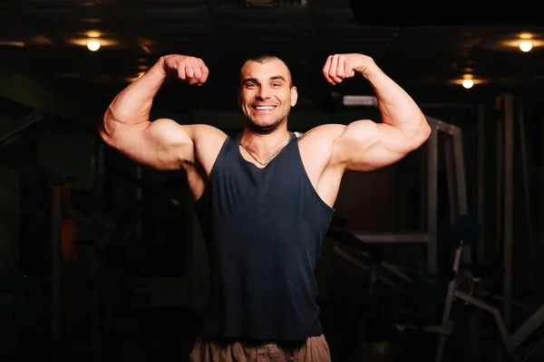 Yakışıklı ve kaslı bir adam, spor salonunda kameraya poz veriyor.