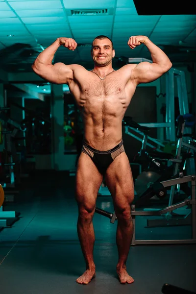 Yakışıklı ve kaslı bir adam, spor salonunda kameraya poz veriyor.