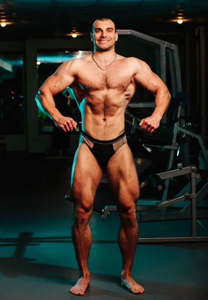 Yakışıklı ve kaslı bir adam, spor salonunda kameraya poz veriyor.