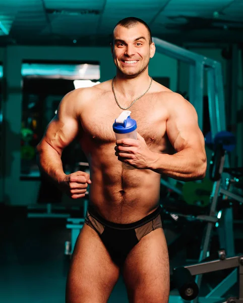 Bonito atlético fitness homem segurando um shaker e posando ginásio — Fotografia de Stock