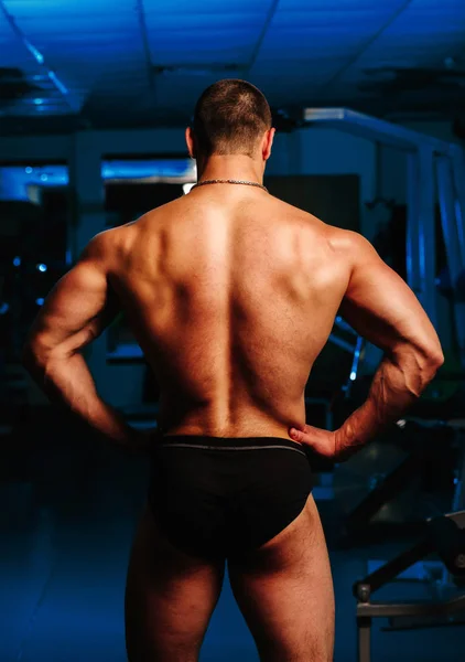 Bodybuilder stands with his back in the gym