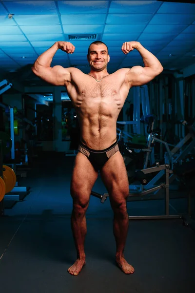 Yakışıklı ve kaslı bir adam, spor salonunda kameraya poz veriyor.