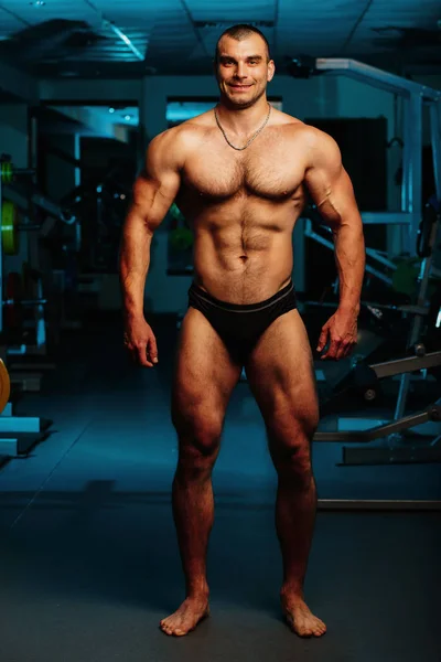 Yakışıklı ve kaslı bir adam, spor salonunda kameraya poz veriyor.