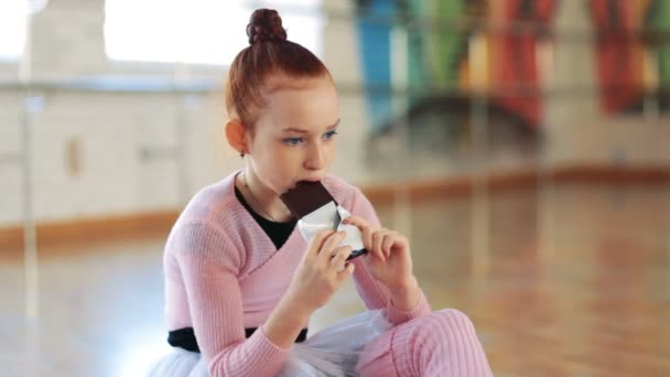 La chica después de un entrenamiento en la sala de ballet come chocolate. La chica junto a la ventana — Vídeo de stock