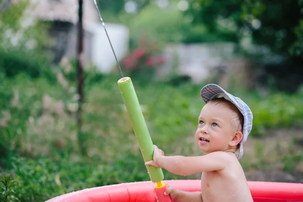 Happy laughing child playing with water gun in outdoor swimming pool on summer vacation in tropical resort. — Stock Photo, Image