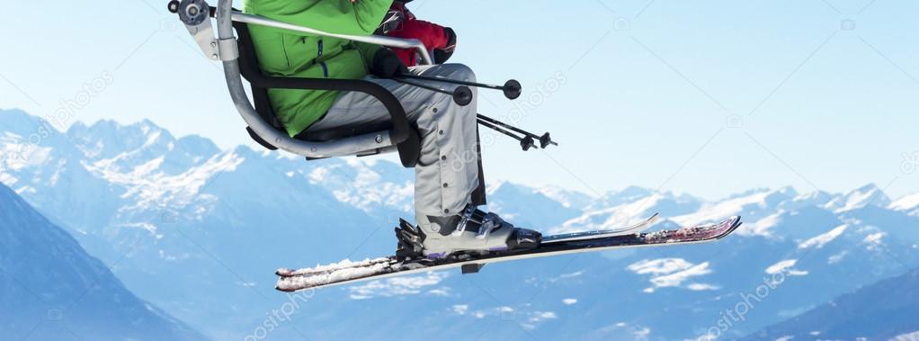 skiers on chairlift with snowy mountains in the background