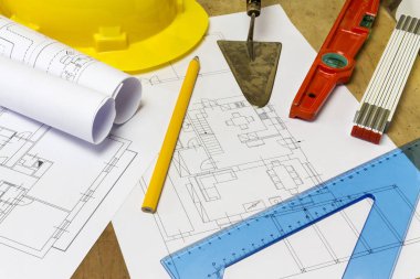 Koruyucu kask, mason araçları ve ahşap arka plan üzerinde proje çizimleri