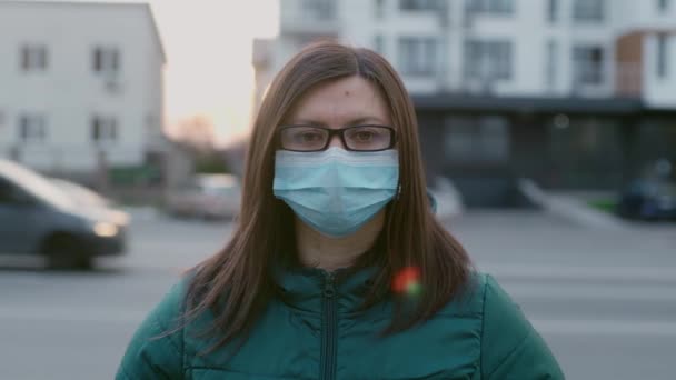 En ung flicka i glasögon och medicinsk mask står på gatan. — Stockvideo