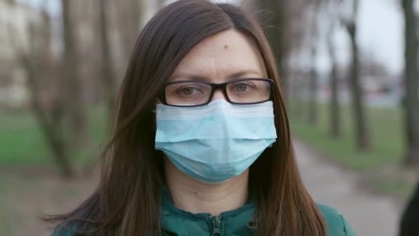 Młoda dziewczyna w okularach i masce medycznej stoi na ulicy. — Wideo stockowe