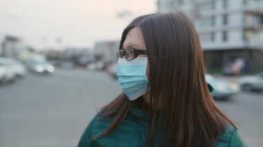 Gözlüklü ve tıbbi maskeli genç bir kız sokakta duruyor. 4k