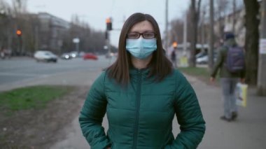 Gözlüklü ve tıbbi maskeli genç bir kız sokakta duruyor..