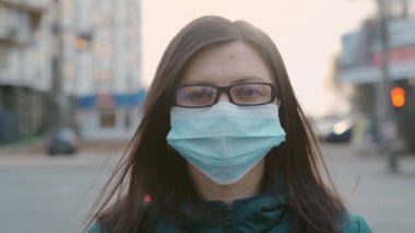 Gözlüklü ve tıbbi maskeli genç bir kız sokakta duruyor. 4k