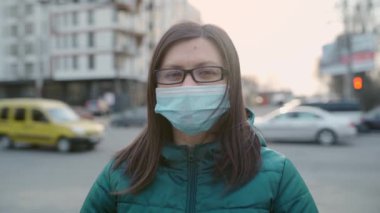 Gözlüklü ve tıbbi maskeli genç bir kız sokakta duruyor. 4k