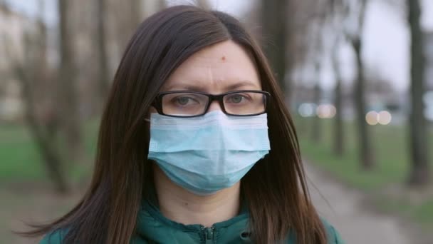 Uma jovem de óculos e máscara médica fica na rua . — Vídeo de Stock