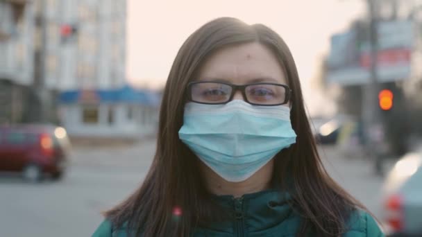 Una giovane ragazza in occhiali e una maschera medica si trova sulla strada. 4k — Video Stock