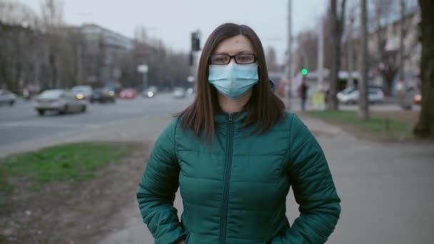 Молодая девушка в очках и в медицинской маске стоит на улице. 4k — стоковое видео