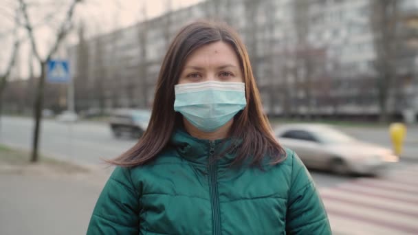 En ung flicka i glasögon och en medicinsk mask står på gatan. 4k — Stockvideo