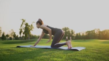 Yeşil çimenlerin üzerinde bir parkta genç bir kız bir tahtada duruyor, gün batımında spor yapıyor..