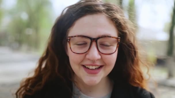 Egy vörös hajú, szemüveges lány portréja, aki a kamerába néz és mosolyog.4k — Stock videók
