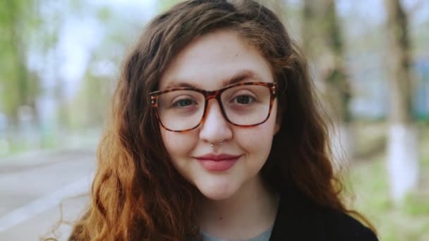 Egy vörös hajú, szemüveges lány portréja, aki a kamerába néz és mosolyog.4k — Stock videók