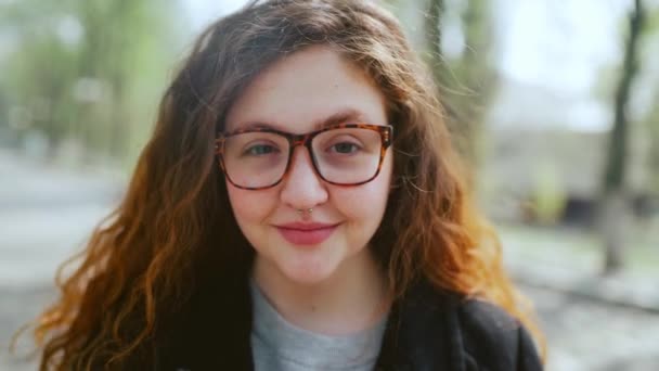 Portret van een roodharig meisje in een bril, kijkend naar de camera en lachend. — Stockvideo