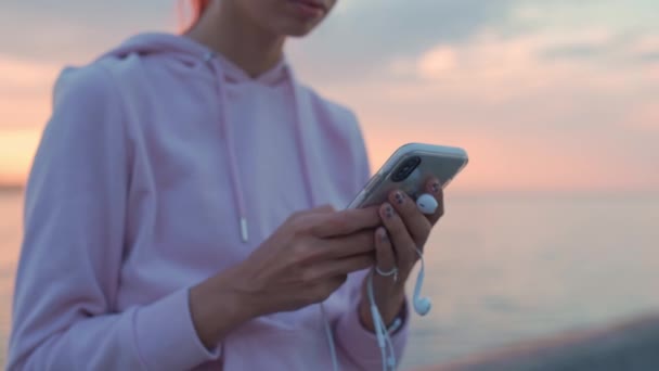 Chica caminando por el paseo marítimo escribe un mensaje en un teléfono inteligente . — Vídeos de Stock