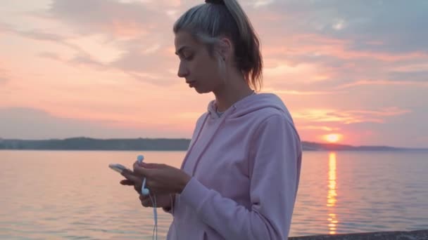 Una jovencita corre por el paseo marítimo, escuchando música con auriculares . — Vídeos de Stock