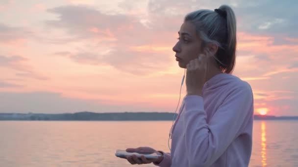 Uma jovem corre ao longo do passeio, ouvindo música com fones de ouvido . — Vídeo de Stock