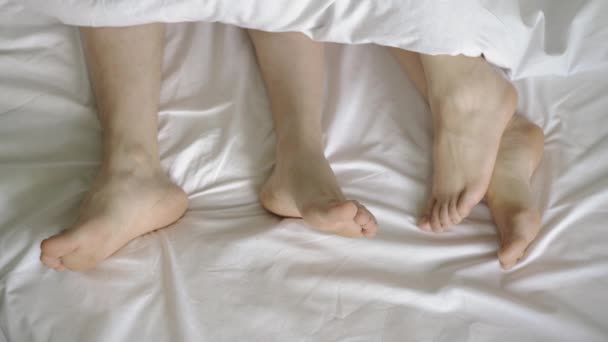 Yatakta bir çift. Erkek ve kadın bacakları beyaz bir yatağın üstünde. 4k — Stok video