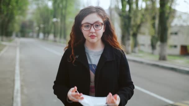 Una joven pelirroja se para en la calle, se pone una máscara médica . — Vídeos de Stock