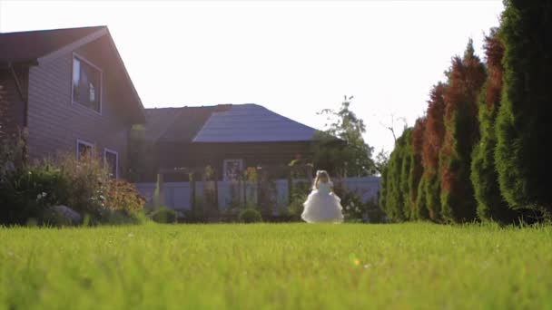 Маленька дівчинка в білому платті ходьба на траві повільний рух — стокове відео
