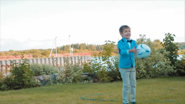 Menino brincando com uma bola no gramado perto do rio — Vídeo de Stock