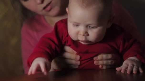Весела дитина з сірими очима досліджує світ сидячи на маминій лапі — стокове відео